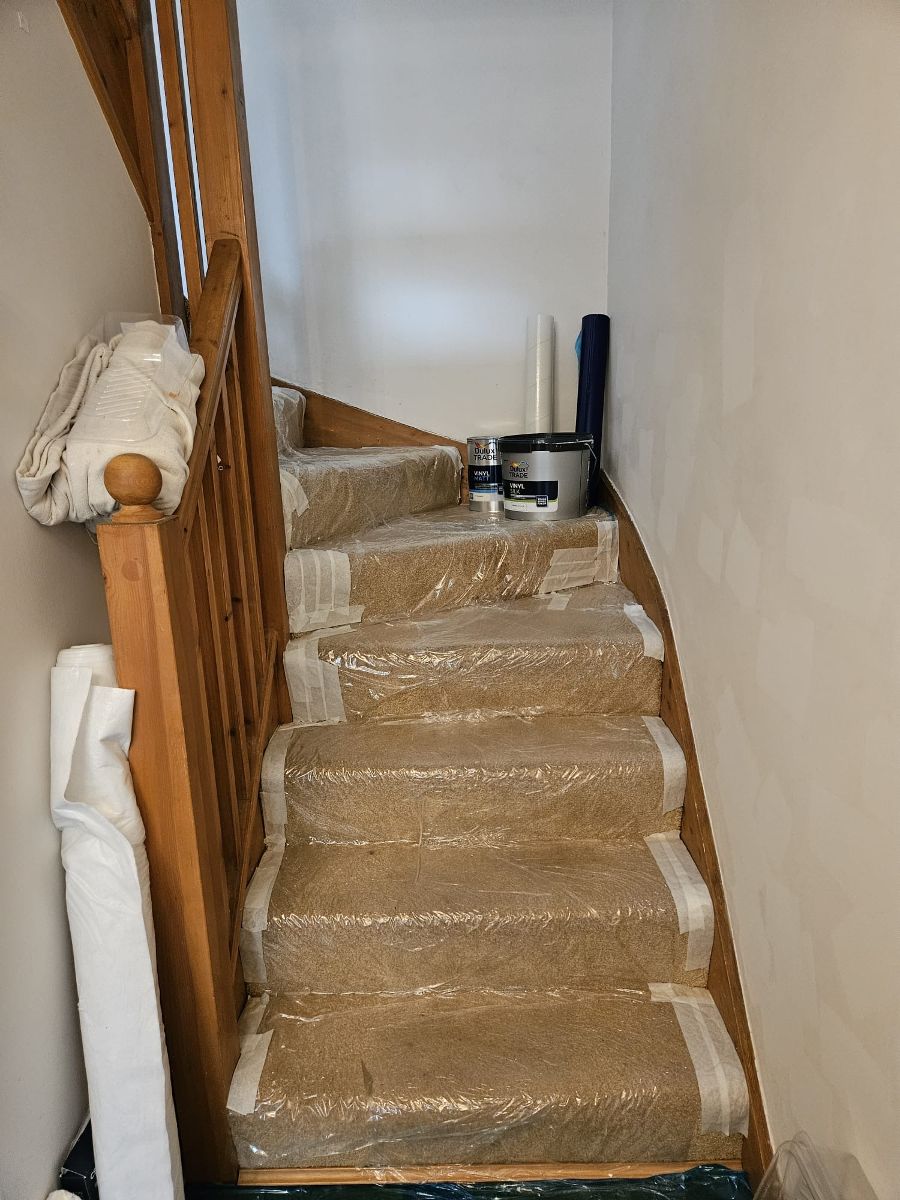 A staircase fully sheeted and taped before painting, with trade paint ready on the landing