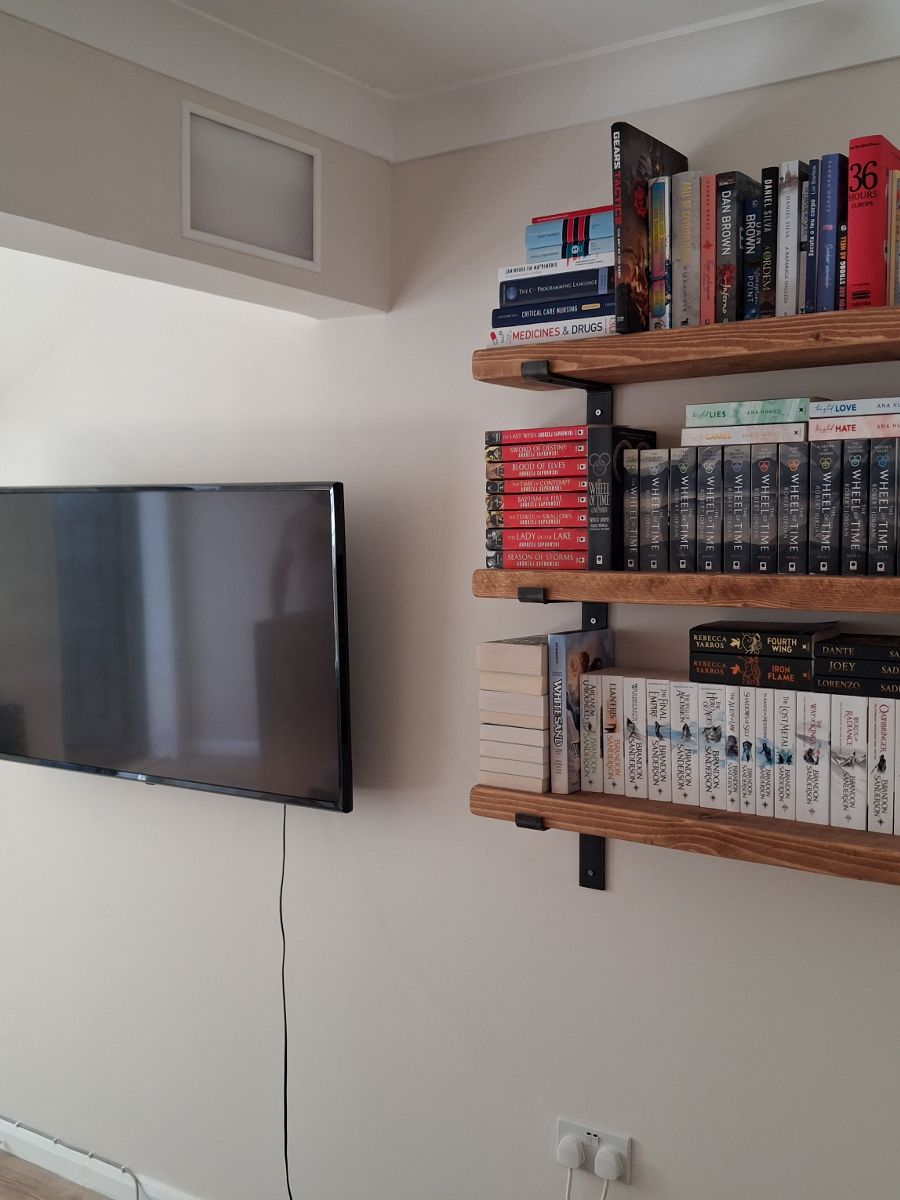 A television mounted flat to a living-room wall beside newly fitted shelves